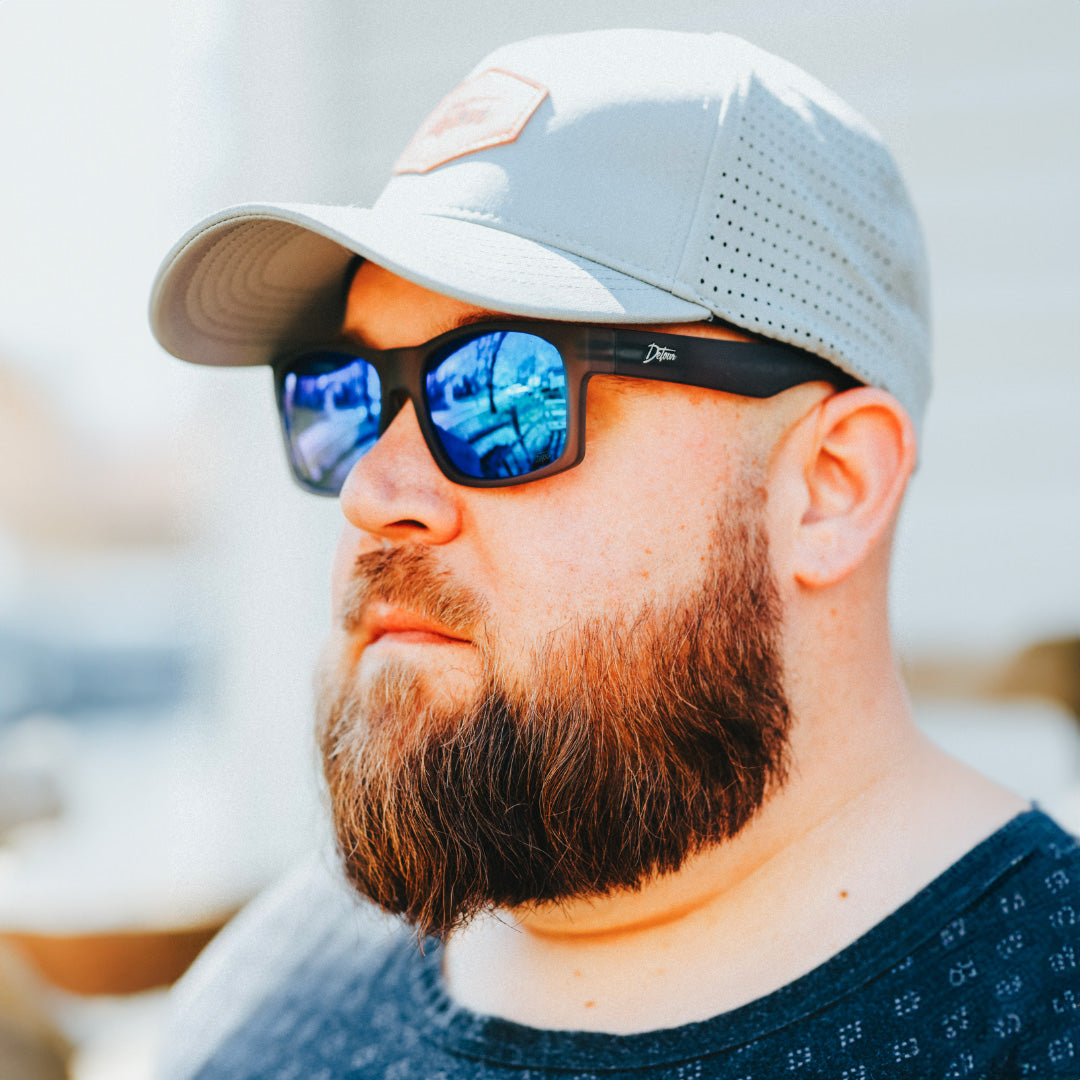 Man wearing mirrored goggles and gray beanie, holding skis in a snowy setting.
