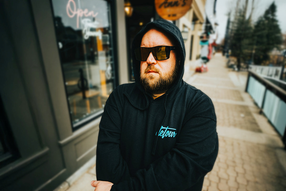 Man wearing mirrored goggles and gray beanie, holding skis in a snowy setting.