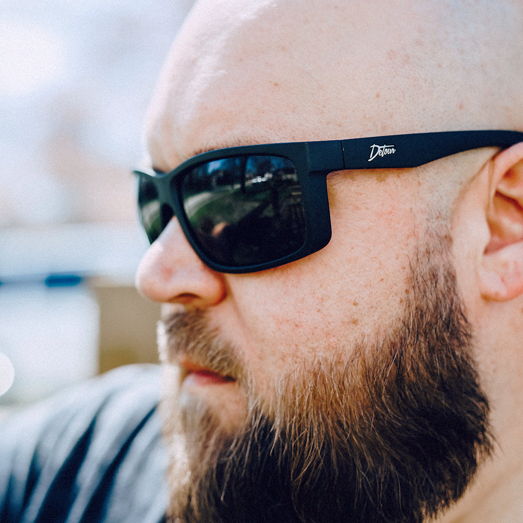 Man wearing mirrored goggles and gray beanie, holding skis in a snowy setting.