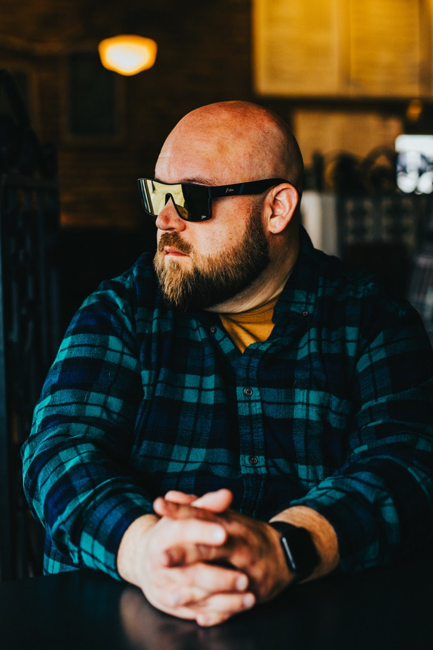 Man wearing mirrored goggles and gray beanie, holding skis in a snowy setting.
