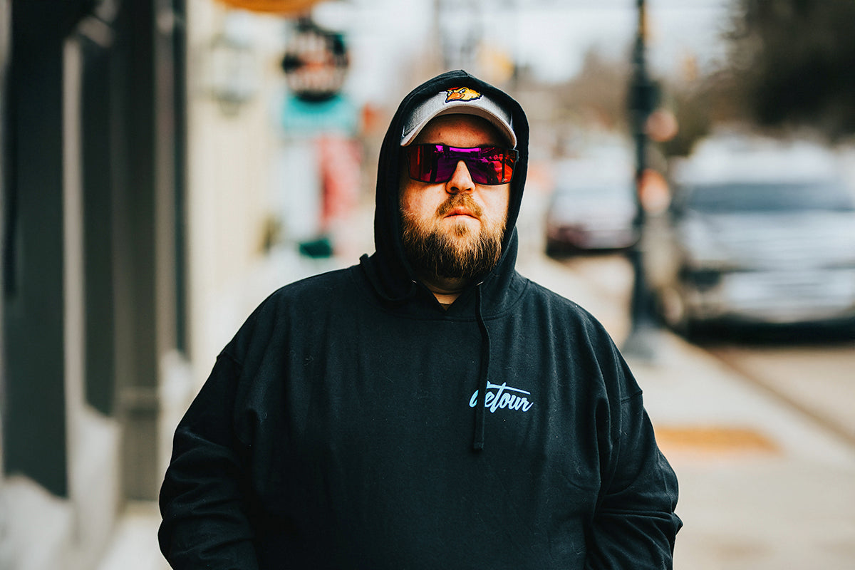 Man wearing mirrored goggles and gray beanie, holding skis in a snowy setting.