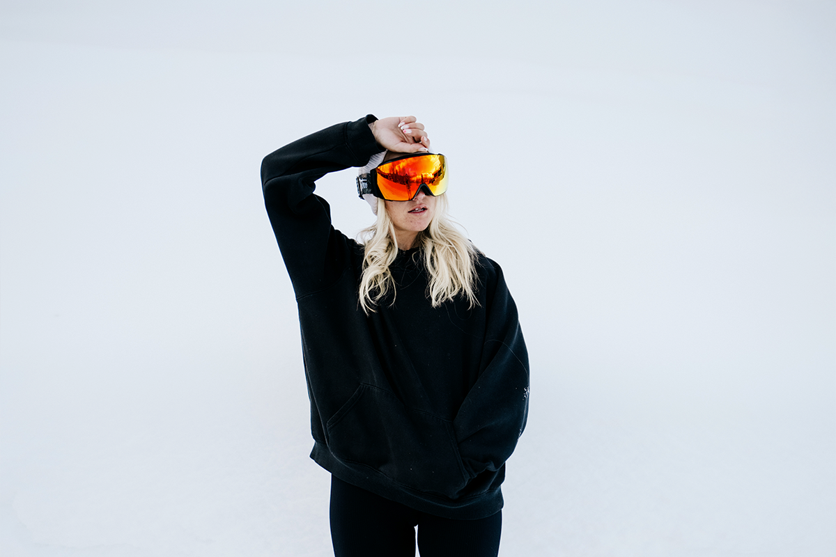 Person in ski gear, reflecting goggles, helmet, snowy landscape in background.