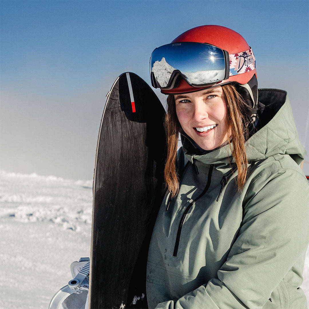 Person holding purple ski goggles with snowy background.